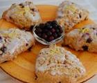 Four blueberry scones with a small bowl of blueberries on a wooden board.