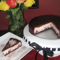 A slice of berry cheesecake on a plate with the remaining cake on a stand.