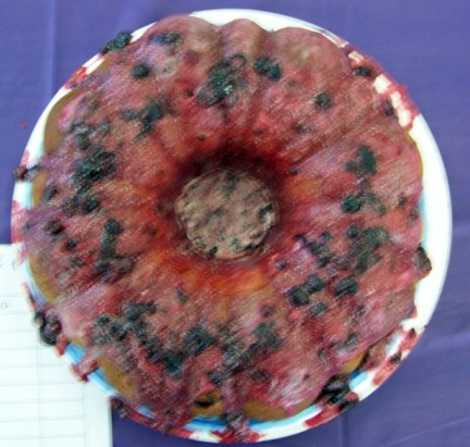 A round cake with dark spots on top, placed on a decorative plate.
