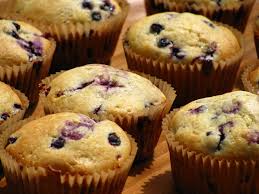 Freshly baked blueberry muffins cooling on a wooden surface.