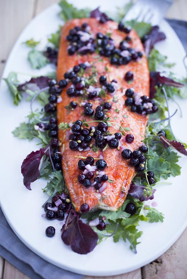 Grilled salmon topped with fresh blueberries on a bed of greens.