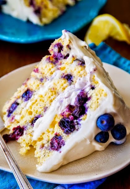 A slice of blueberry cake with creamy frosting on a plate.
