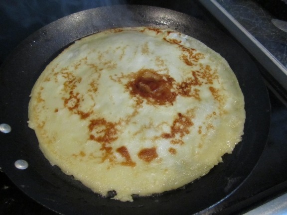 A pancake cooking on a black griddle.