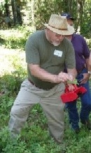 Man examining plant outdoors with magnifying tool.