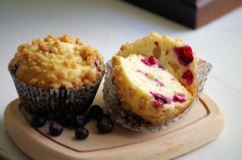 Two muffins, one with blueberries and one with cranberries, on a wooden board.