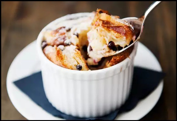 A warm bread pudding served in a white ramekin with a spoon.