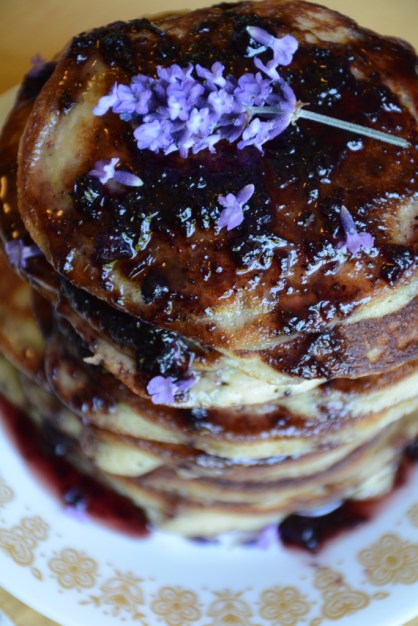 Stack of pancakes topped with syrup and purple flowers.