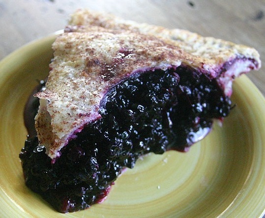 A slice of blueberry pie with juicy filling on a plate.