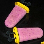 Two purple homemade popsicles with yellow handles on a black background.