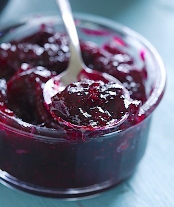 A spoonful of dark purple jam in a glass jar.