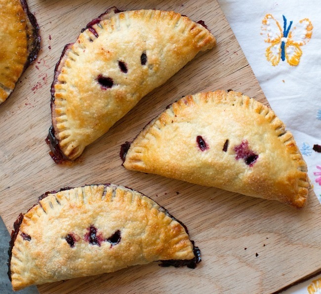 Three golden-brown fruit-filled hand pies on a wooden board.