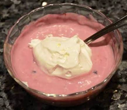 A bowl of pink yogurt topped with whipped cream and a spoon.