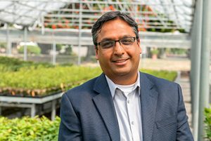Man in suit smiling at greenhouse.