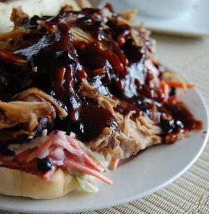 Pulled pork sandwich topped with barbecue sauce on a plate.