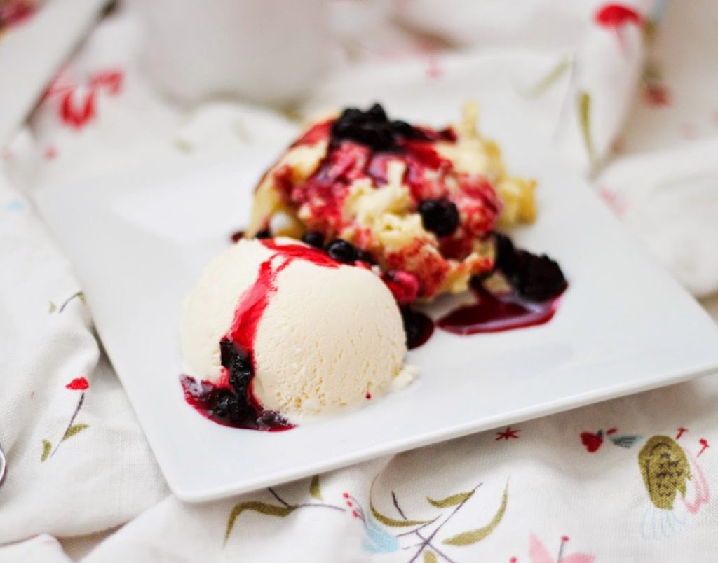 A scoop of vanilla ice cream with berry sauce and a fruit crumble.