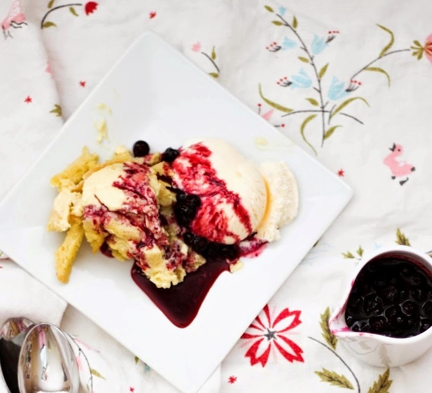 A dessert with ice cream, berry sauce, and a crumble topping on a white plate.