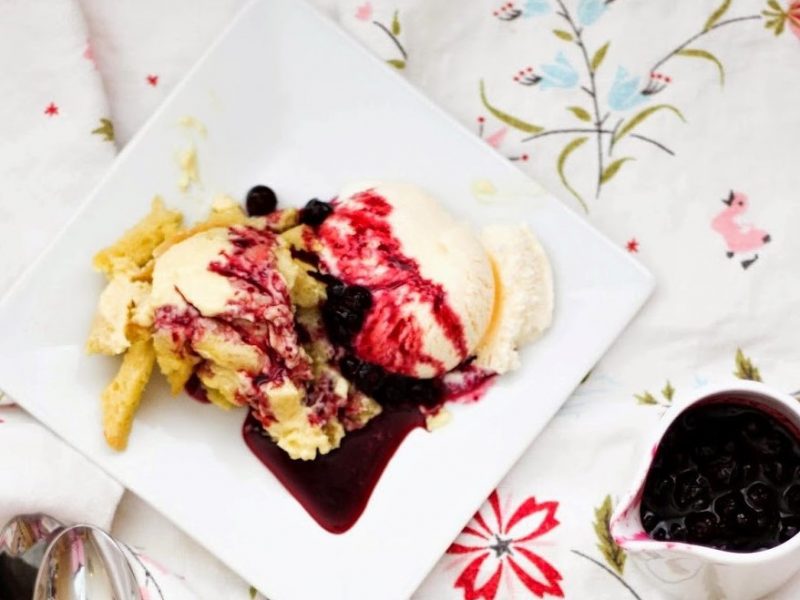 Dessert with vanilla ice cream, berry sauce, and nuts on a white plate.