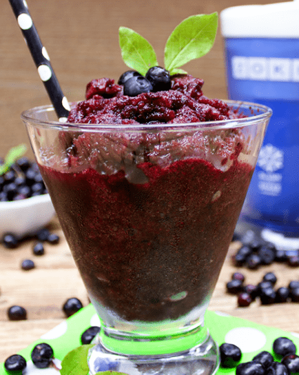 A glass of mixed berry dessert with a spoon.