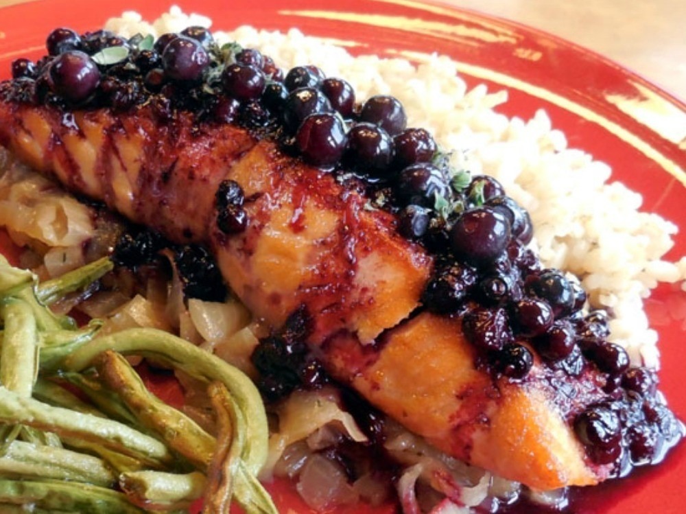 Grilled salmon topped with a blueberry glaze, served with rice and green beans.