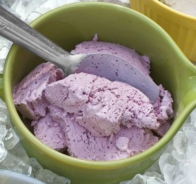 A scoop of purple ice cream in a green cup with a spoon.
