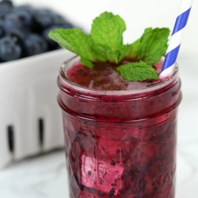 A refreshing blueberry smoothie in a mason jar with a mint garnish and striped straw.