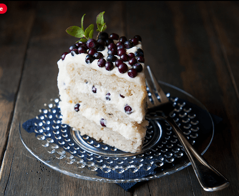 Slice of vanilla cake with blueberries and cream on a glass plate.